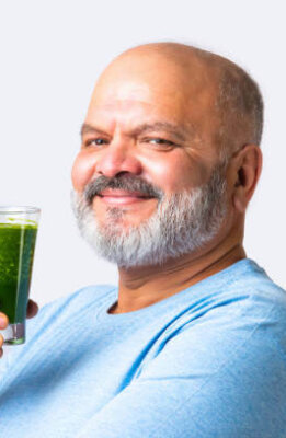 Indian Asian elderly old senior man drinking an organic green smoothie or juice in a glass